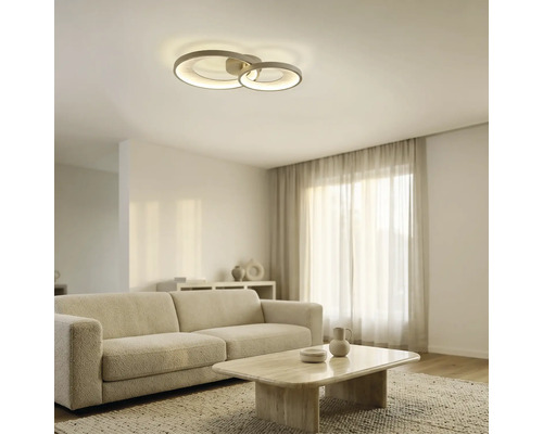 Moderne LED-Deckenleuchte mit zwei ineinandergreifenden Ringen in einem hellen, modern eingerichteten Wohnzimmer mit Sofa und Couchtisch.