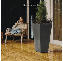 Jardinière haute et conique en anthracite sur une terrasse en bois à côté d'une personne assise. Logo Tierra Verde.