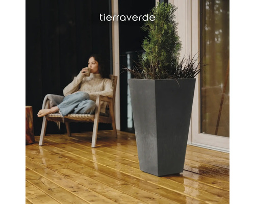 Jardinière haute et conique en anthracite sur une terrasse en bois à côté d'une personne assise. Logo Tierra Verde.