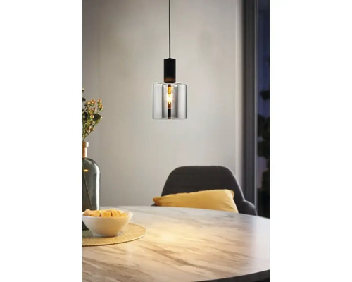 Moderne Pendelleuchte mit zylindrischem Glasschirm und schwarzer Metallfassung über einem Esstisch in Marmoroptik.