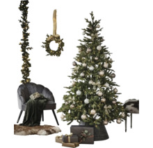 Festlich dekorierter Weihnachtsbaum im Korb, grauer Samtsessel mit Decke, Fellteppich, Geschenke sowie Kranz und Girlande an der Wand.