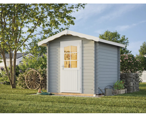 Abri de jardin classique en bois gris avec porte blanche et bordure de toit décorée dans un jardin verdoyant.