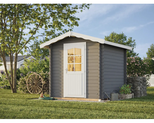 Abri de jardin gris en bois avec toit à deux pans blanc et porte blanche avec fenêtre à croisillons, situé dans un jardin avec une roue de charrette.