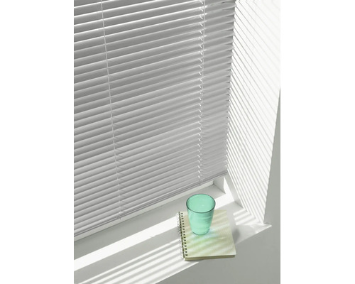Jalousie mit horizontalen Lamellen vor einem hellen Fenster, die Schatten auf eine Fensterbank mit Glas und Notizblock wirft.