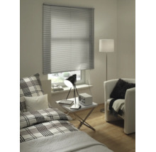 Modernes Zimmer mit silberner Aluminium-Jalousie am Fenster, Bett mit Karomuster, weißem Beistelltisch und Sessel.