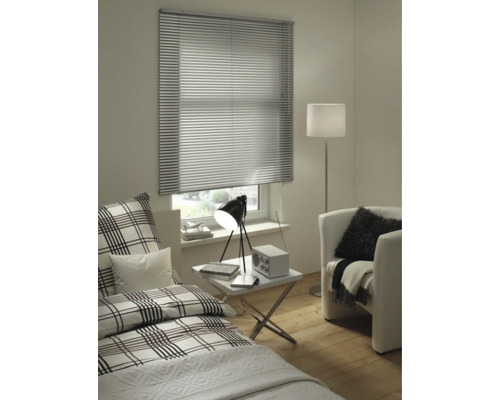 Modernes Zimmer mit silberner Aluminium-Jalousie am Fenster, Bett mit Karomuster, weißem Beistelltisch und Sessel.