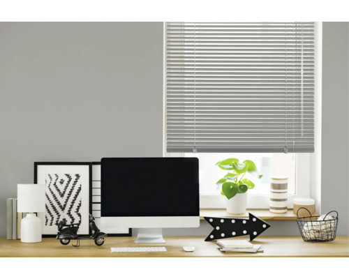 Eine horizontale Jalousie an einem Fenster über einem modern eingerichteten Schreibtisch mit Monitor, Lampe und Dekoration im Arbeitszimmer.