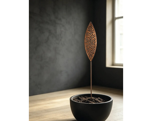 Pic de jardin en métal en forme de feuille avec découpes florales dans un pot noir, dans un environnement moderne et minimaliste.