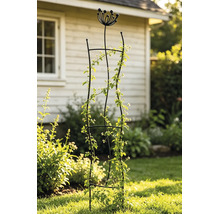 Support de jardin en métal noir avec un sommet décoratif en forme de fleur, portant une plante grimpante dans un jardin ensoleillé.