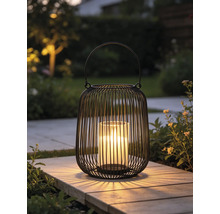 Lanterne moderne en fil métallique noir avec insert en verre et bougie allumée sur une dalle de jardin.