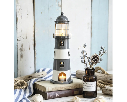 Photophore décoratif en forme de phare, gris et blanc, utilisé comme bougeoir sur des livres dans un décor maritime.