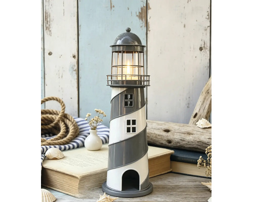 Porte-bougie chauffe-plat décoratif en forme de phare avec motif en spirale et bougie allumée dans une scène maritime avec corde, livres et coquillages.