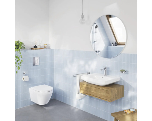 Salle de bain moderne et lumineuse avec WC suspendu, lavabo blanc sur meuble sous-vasque en bois, miroir rond et carrelage mural bleu clair.