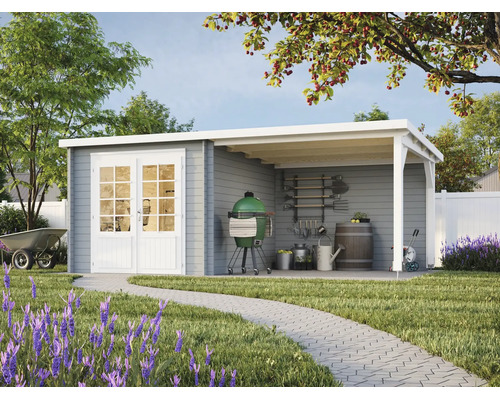Abri de jardin en bois gris avec toit en appentis, double porte blanche et grand auvent de terrasse dans un jardin avec pelouse et allée pavée.