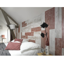 Chambre mansardée avec papier peint aspect bois, lit avec coussins, lampadaire et poutres en bois apparentes.