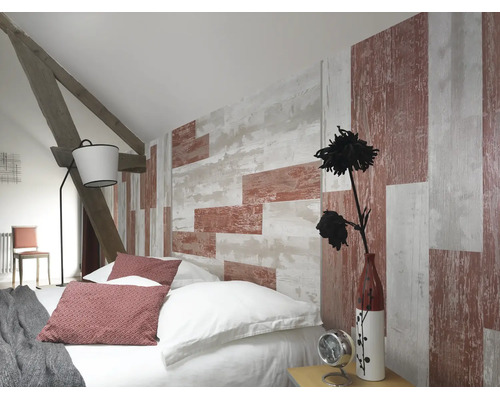Chambre mansardée avec papier peint aspect bois, lit avec coussins, lampadaire et poutres en bois apparentes.