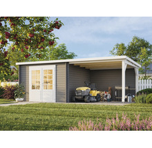 Abri de jardin moderne en bois gris avec doubles portes blanches et auvent. Sous l'auvent se trouvent un tracteur tondeuse et des outils.
