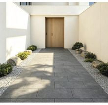 Entrée moderne avec une allée en grandes dalles de terrasse grises, bordée de gravier blanc, de petits arbustes et de pierres.