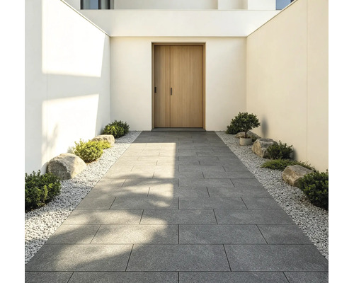 Entrée moderne avec une allée en grandes dalles de terrasse grises, bordée de gravier blanc, de petits arbustes et de pierres.