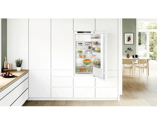 Cuisine équipée moderne avec réfrigérateur encastrable dans une atmosphère lumineuse et ouverte avec parquet.