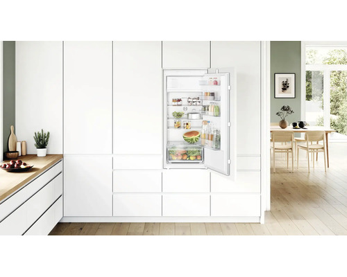 Réfrigérateur encastrable Bosch dans une cuisine moderne et lumineuse, porte ouverte avec étagères et bac à fruits remplis.