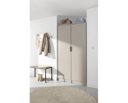 Entrée moderne avec armoire beige à deux portes, banc en bois, patères sur mur blanc et tapis rond.