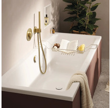 Baignoire moderne avec robinetterie encastrée et douchette dorées, incluant un support en métal avec un livre et une éponge dans une salle de bain.