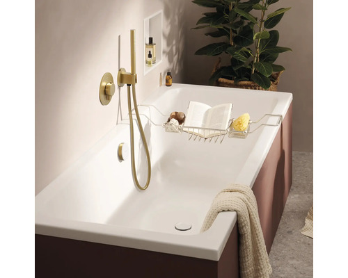 Baignoire moderne avec robinetterie encastrée et douchette dorées, incluant un support en métal avec un livre et une éponge dans une salle de bain.