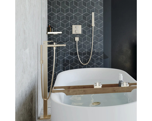 Salle de bain moderne avec baignoire îlot, mitigeur de baignoire sur pied et robinetterie encastrée avec douchette devant des carreaux géométriques.