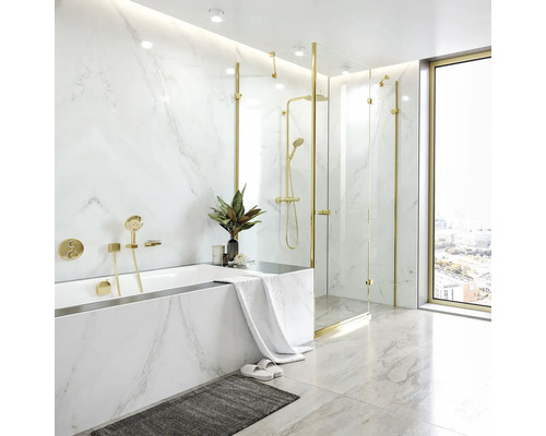 Modernes Badezimmer mit Marmoroptik Fliesen, Badewanne, bodengleicher Glasdusche und goldenen Armaturen bei Tageslicht.