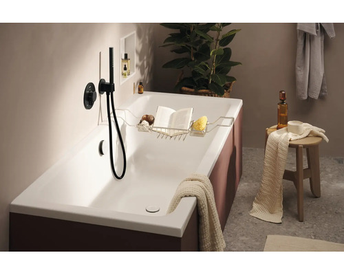Baignoire moderne avec tablette, livre, éponge et mitigeur. Ambiance de salle de bain élégante avec serviette et tabouret de rangement.