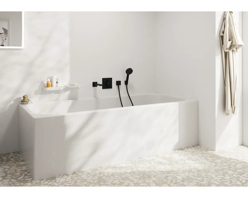 Salle de bain moderne avec baignoire blanche, robinetterie encastrée et douchette dans une pièce au sol en terrazzo clair au design minimaliste.