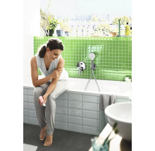 Femme assise sur le bord d'une baignoire dans une salle de bains moderne avec des mosaïques vertes et un mitigeur de baignoire avec douchette.