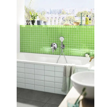 Salle de bain moderne avec baignoire blanche, robinetterie, carrelage en mosaïque vert et fenêtre avec vue sur la ville.