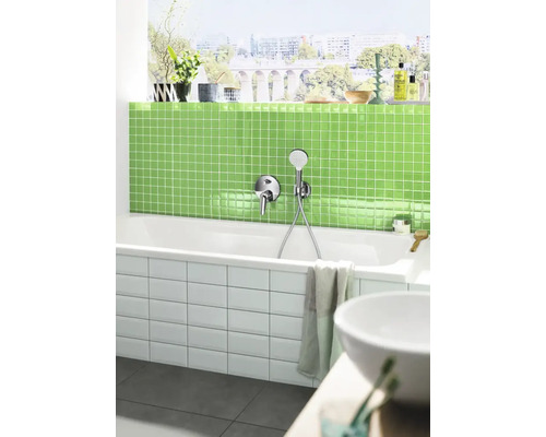 Salle de bain moderne avec baignoire blanche, robinetterie, carrelage en mosaïque vert et fenêtre avec vue sur la ville.