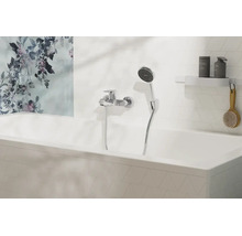 Mitigeur de baignoire moderne avec douchette sur un mur carrelé blanc au-dessus d'une baignoire avec une fresque florale.