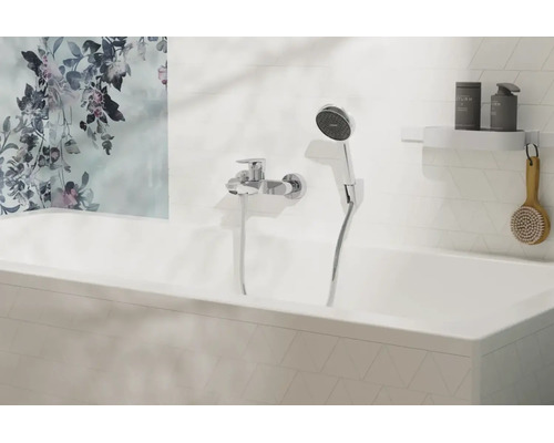 Mitigeur de baignoire moderne avec douchette sur un mur carrelé blanc au-dessus d'une baignoire avec une fresque florale.