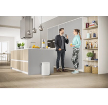 Cuisine moderne avec îlot central, une poubelle blanche au premier plan et un couple en conversation.