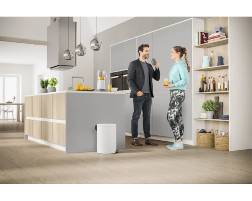 Cuisine moderne avec îlot central, une poubelle blanche au premier plan et un couple en conversation.