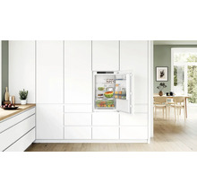 Réfrigérateur encastrable dans une cuisine moderne blanche avec porte ouverte et étagères remplies.