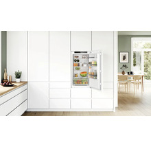 Réfrigérateur encastrable dans une cuisine moderne blanche avec porte ouverte, étagères et bac à légumes remplis.