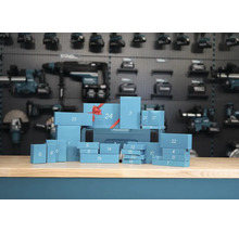 Calendrier de l'avent d'outils Makita avec vingt quatre boîtes cadeaux numérotées sur un établi devant un mur d'outils.