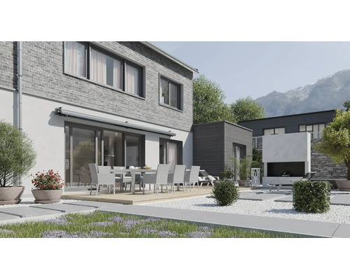 Terrasse moderne avec coin repas devant une maison en briques avec store et cheminée extérieure dans un jardin soigné avec vue sur la montagne.
