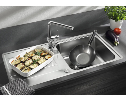 Évier de cuisine moderne en acier inoxydable avec robinet intégré, égouttoir, un plat à four et une poêle dans une cuisine fonctionnelle.