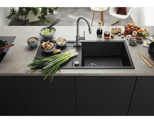 Évier encastrable noir moderne avec égouttoir et robinet en acier inoxydable dans une cuisine organisée avec des ingrédients frais sur le plan.