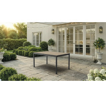 Table de jardin avec plateau en bois et cadre en métal sur une terrasse pavée devant une maison avec de grandes portes-fenêtres.