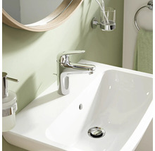 Mitigeur de lavabo moderne en chrome sur un lavabo blanc dans une salle de bains avec miroir et accessoires.