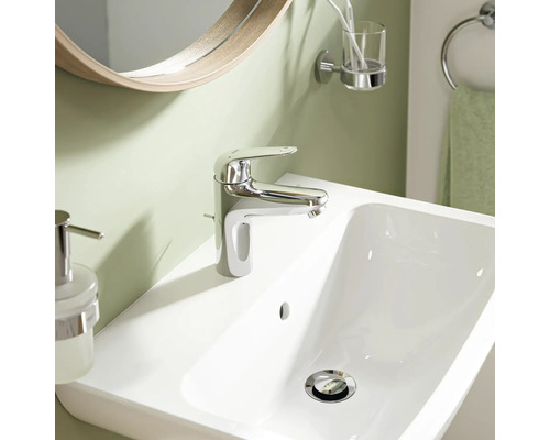 Mitigeur de lavabo moderne en chrome sur un lavabo blanc dans une salle de bains avec miroir et accessoires.