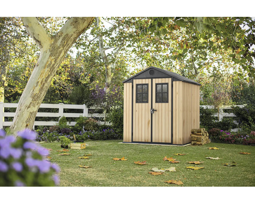 Abri de jardin en bois et métal dans un jardin avec pelouse sous des arbres.