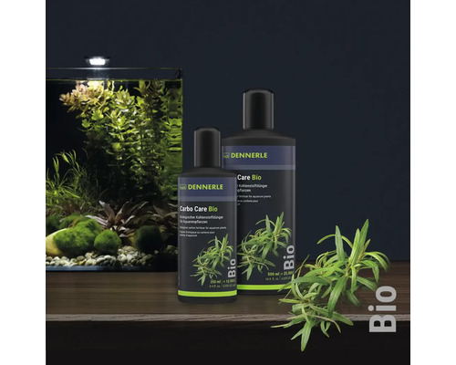 Dennerle Carbo Care Bio Pflanzendünger in zwei Flaschengrößen neben einem bepflanzten Aquarium.